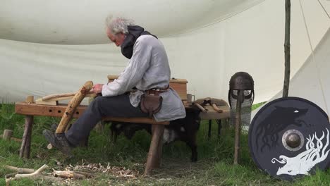 Viking-re-enactment-wood-worker-in-period-clothes-crafting-wood-into-a-implement-at-Woodstown-Waterford-Ireland