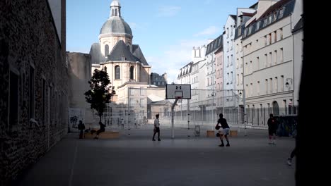 Kinder-Spielen-Basketball-Auf-Dem-Hinterhofplatz-Von-Paris:-Nachbarschaftsstimmung-Mit-Blick-Auf-Die-örtliche-Kirche,-Sport-Und-Gemeinschaft-Im-Städtischen-Umfeld