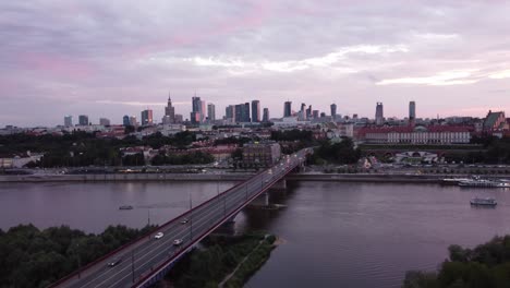 Drohnenaufnahmen-Der-Warschauer-Skyline-Und-Der-Weichsel-Mit-Einer-Brücke-Bei-Einem-Magischen-Rosa-Sonnenuntergang-Mit-Filmischem-Rollback