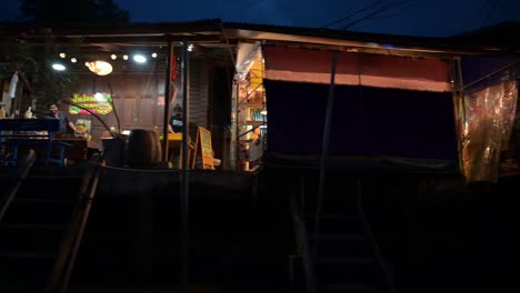 Moving-from-right-to-the-left-as-the-boat-is-cruising-along-the-canals-of-Amphawa-Floating-Market-on-a-night-tour-in-Mae-Klong-River-in-Samut-Songkhram,-Thailand