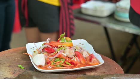 Alejándose-Del-Encuadre-En-Un-Plato-Lleno-De-Ensalada-De-Papaya-Tailandesa-Somtam,-Tomada-Por-Un-Cliente-Desde-La-Izquierda-De-Un-Vendedor-Ambulante-Local-En-Las-Calles-De-Bangkok,-Tailandia.