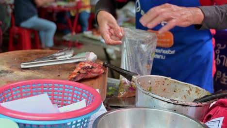 Vendedor-Ambulante-Local-Empacando-Los-Pedidos-De-Los-Clientes-De-Carne-Picada-Picante-Llamada-Laab-Y-Algo-De-Cerdo-Asado-En-Una-Bolsa-En-Un-Restaurante-Local-En-Las-Calles-De-Bangkok,-Tailandia