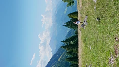 Wide-shot-of-happy-girl-running-and-turning-on-green-slope-of-alp-mountains-during-sunny-day---vertical-shot