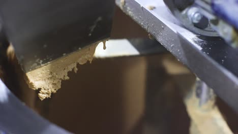 Slow-motion-close-up-scene-of-peanut-butter-being-ground-into-cream-in-a-peanut-butter-processing-plant-and-machine-cutting-the-peanut-cream-and-storing-it-in-a-storage-tank