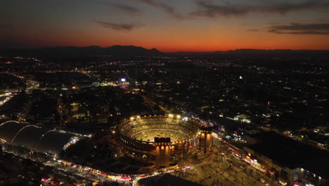 Aerial-view-around-the-illuminated-Plaza-de-Toros,-bullfighting-arena,-dusk-in-Aguascalientes,-Mexico