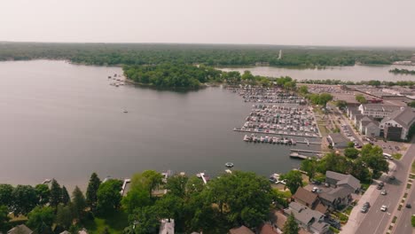Aerial-drone-shot-of-lake-shoreline-with-a-boat-harbor-and-multiple-boats-at-the-docks