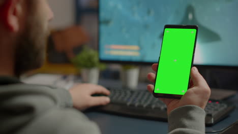 Competitive-gamer-looking-at-smartphone-with-green-screen-display