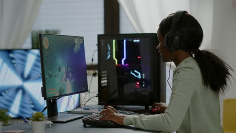 Excited-black-woman-gamer-sitting-on-desk,-having-headset-with-mic-playing