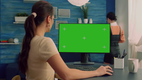 Caucasian-female-typing-on-professional-computer-with-mock-up-green-screen-chroma-key-display