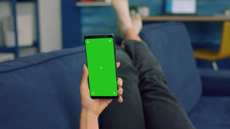 Freelancer-woman-lying-on-sofa-looking-at-mock-up-green-screen-chroma-key-smartphone