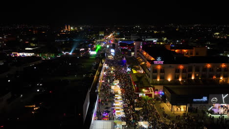 Drone-shot-panning-over-blinking-night-lit-streets-of-Aguascalientes,-during-the-San-Marcos-fair