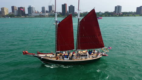 Drone-shot-following-an-old-sailboat,-sailing-on-the-Detroit-river-with-Canada-in-the-background
