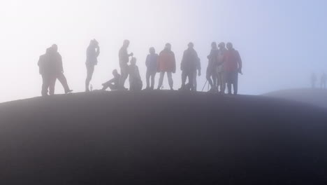 Group-of-hikers,-stand-in-cloud-silhouette-on-top-of-mountain-volcano
