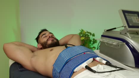 Male-latin-mexican-guest-patient-muscle-handsome-guy-receive-treatment-procedure-of-lipo-laser-energy-no-pain-lay-down-at-spa-hotel-wellness-center-enjoy-relax