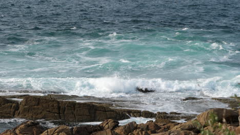 Slow-Motion-Shot-of-Ocean-Waves-Breaking-on-Rocky-Shoreline,-Sunny-Day