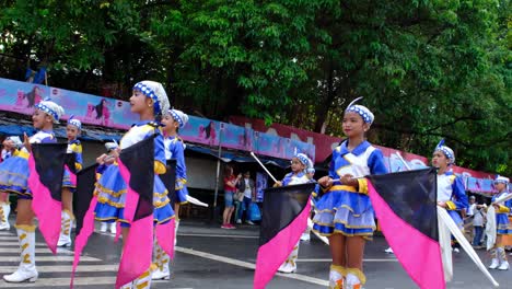 Un-Grupo-De-Jóvenes-Vestidas-Con-Trajes-Coloridos-Y-Portando-Una-Pancarta-En-La-Calle-Para-El-Desfile-En-La-Ciudad-De-Davao,-Filipinas