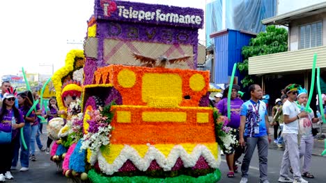 A-car-that-is-decorated-with-with-yellow-and-orange-flowers-on-the-road-with-people-walking-on-the-each-side