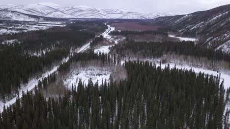 Nach-Oben-Geneigter-Luftblick-über-Die-Wildnis-Alaskas,-Schneebedeckte-Hügel-Im-Hintergrund,-Gefrorener-Fluss-Und-Teich