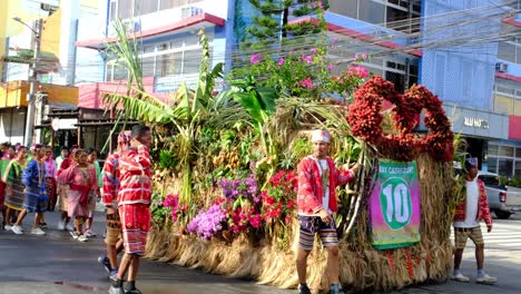 A-vehicle-decorated-with-fruits,-vegetables,-and-flowers-with-tribes-walking-on-each-side