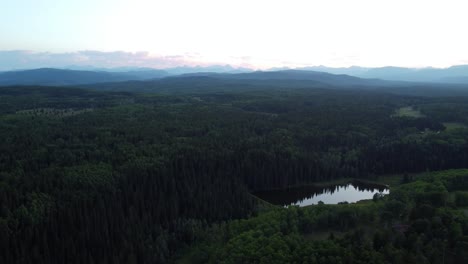 Drohne-Fliegt-Bei-Sonnenuntergang-über-Einem-Stimmungsvollen-Wald-Mit-Den-Felsigen-Bergen-Im-Hintergrund-In-Kanada