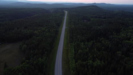 Revealing-aerial-shot-of-the-highway-in-the-Canadian-Rocky-Mountains-surrounded-by-forest-in-summertime