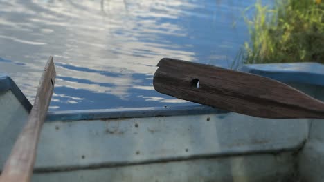 Paddles-against-boat-on-shore-by-calm-water,-boat-by-lake-oars-close-up