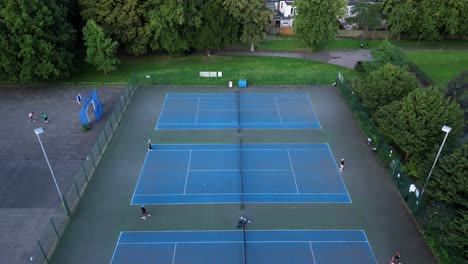 Atletas-Entrenando-Y-Practicando-Tenis-En-Canchas-Azules-Al-Aire-Libre,-Aéreas