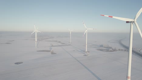 Several-wind-turbines-in-winter-landscape-near-highway-on-a-sunny-day,-aerial-drone-view