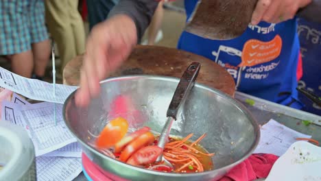 Local-street-cook-making-vegetable-salad-with-tomatoes,-shredded-carrots,-onions,-coriander-with-some-spices-and-condiments-in-a-roadside-restaurant-in-Bangkok,-Thailand