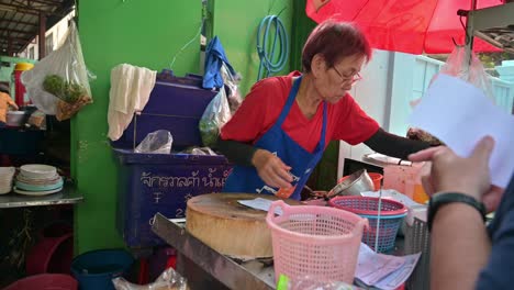 Bangkok-street-hawker-reading-the-orders-of-her-customers-for-grilled-chicken-and-pork-that-she-needs-to-prepare