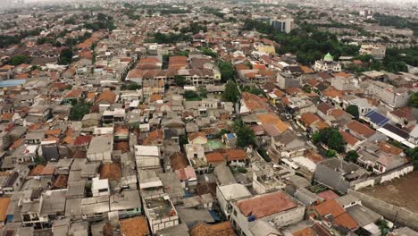 Aerial-tilt-up-of-crowded-slum-district-of-Jakarta-during-cloudy-day,-overview-shot-with-skyline-in-backdrop