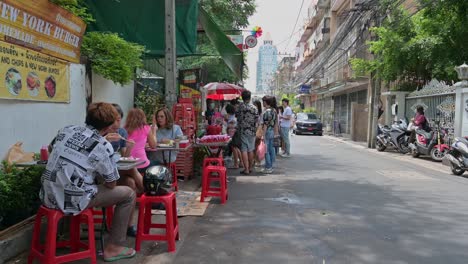 Eating-by-the-roadside,-local-people-and-foreigners-eating-the-famous-Somtam-Thai-papaya-salad-and-grilled-meat,-while-some-are-still-waiting-for-their-orders-in-the-street-of-Bangkok,-Thailand