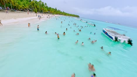Fpv-drone-flight-over-sandy-beach-and-turquoise-Caribbean-sea-water-with-many-swimming-people-on-Saona-Island,-Dominican-Republic
