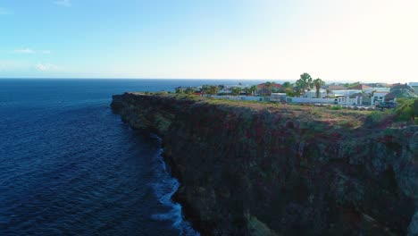 Drone-rises-above-rocky-grey-cliffs-to-luxury-homes-overlooking-beautiful-caribbean-waters,-curacao