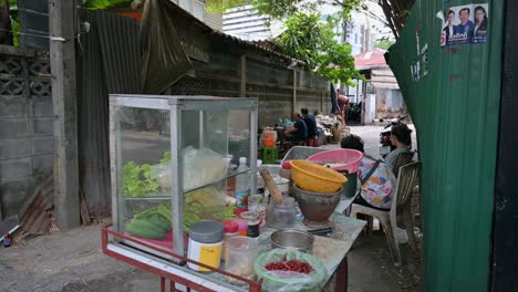 Some-customers-waiting-for-their-orders-while-sitting-on-plastic-stools,-while-others-are-already-eating-at-tables-that-can-be-seen-on-the-far-center-side-of-the-frame