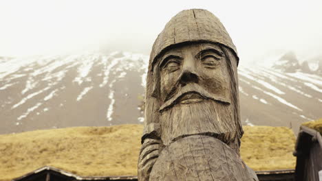 Große-Holzskulptur-Eines-Wikingerkopfes-Unter-Schneebedeckten-Bergen,-Parallaxenschuss