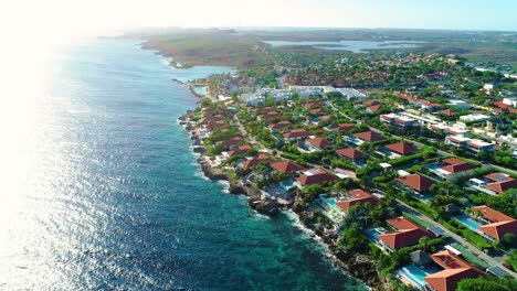 Drone-overview-of-luxury-villas-on-shoreline-of-curacao,-tropical-vacation-at-sunrise