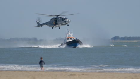 Person-An-Der-Winde-Unter-Dem-Hubschrauber,-Der-über-Dem-SAR-Rettungsboot-Auf-See-Fliegt