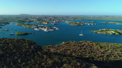 Panoramic-aerial-of-Spanish-Waters-in-Curacao,-with-hill-and-catamaran-during-golden-hour-sunset