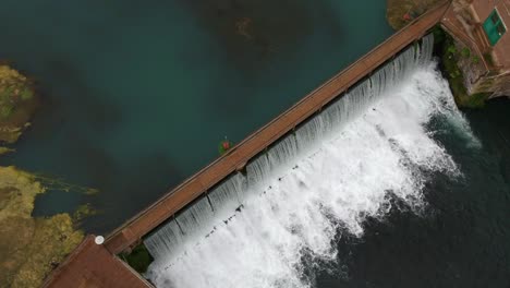 Staudamm-Wasserfall-–-Von-Oben-Nach-Unten-Rotierender-Drohnenwinkel,-Der-Stilles-Und-Rauschendes-Wasser-Zeigt