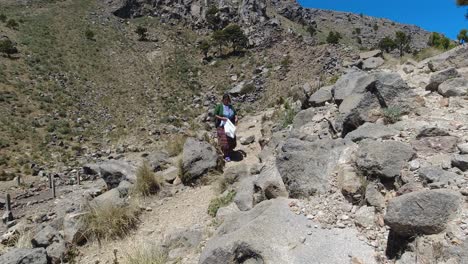 Local-Mayan-woman-walks-down-dry-mountain-path-in-Guatemala,-sunny-day