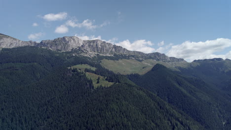 Aerial-view-of-a-high-rocky-mountain-surrounded-by-deep-valleys-with-green-fir-forests-on-a-day-with-blue-sky-and-few-clouds