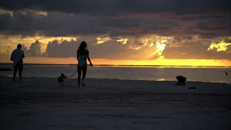 Eine-Lateinamerikanische-Frau-Läuft-Mit-Ihrem-Hund-Am-Strand-Bei-Einem-Faszinierenden-Sonnenuntergang-Am-Strand-In-Cancun,-Mexiko