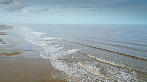 Aerial-video-footage-of-a-coastal-beach-scene-with-ocean,-sand-dunes-and-crashing-waves