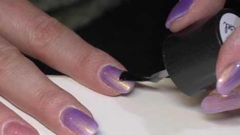 Macro-shot-of-woman-applying-fresh-purple-colored-paint-on-nail-of-finger