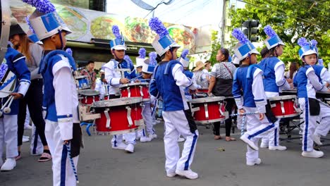 Grupo-De-Jóvenes-Músicos-En-Uniforme-Azul-Y-Blanco-Tocando-Música-Con-Tambores-En-Formación-De-Desfile-Callejero