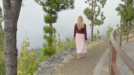 Attractive-blonde-walking-on-top-of-mountain-pathway,-back-view
