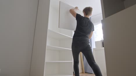 Young-person-install-shelves-into-new-modern-closet,-back-view