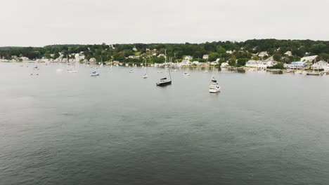 Aerial-view-of-coastal-town-approaching-sail-boats-and-vessels-over-bay-water-in-Rhode-Island