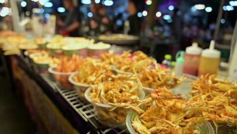 Panning-the-camera-quickly-from-right-to-the-left,-an-array-of-different-fried-foods-can-be-seen-on-display-in-a-food-stall-inside-the-Chatuchak-Weekend-Night-Market-in-Bangkok,-Thailand
